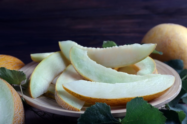 Fatias de melões maduros com folhas verdes na mesa fecham