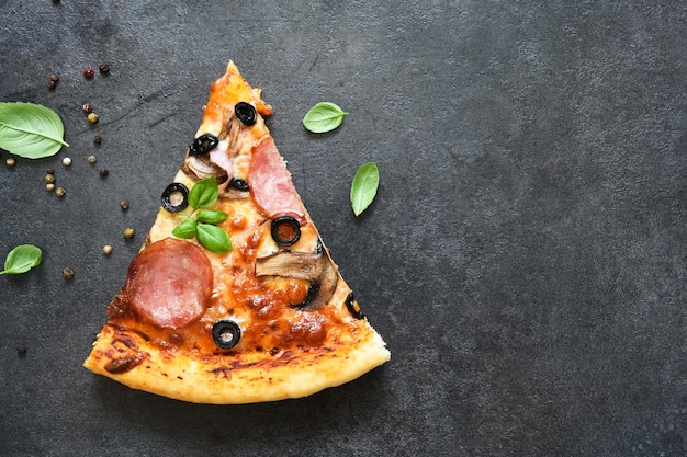 Fatias de pizza com azeitonas de cogumelos salame e manjericão em um fundo preto Vista superior