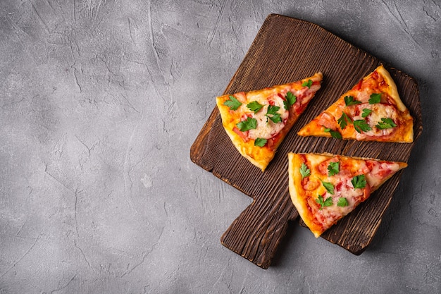 Fatias de pizza quente com queijo mussarela, presunto, tomate e salsa na tábua de madeira marrom