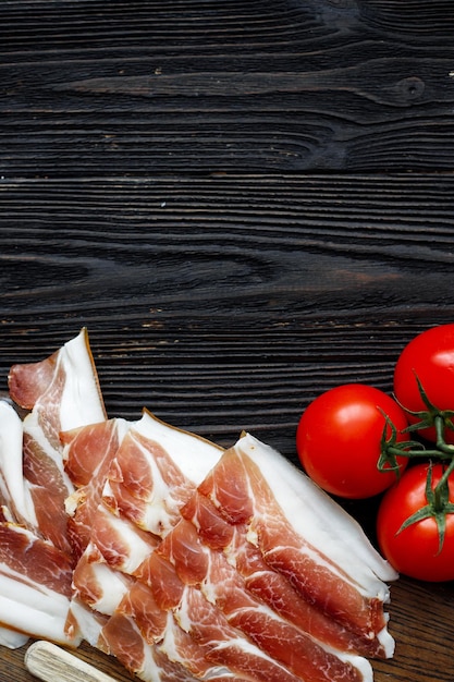 Fatias de presunto de Parma em fundo escuro de madeira com vista superior de tomate postura plana