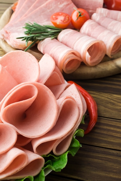 Foto fatias de presunto fresco com lattuce e tomate cereja na placa de madeira