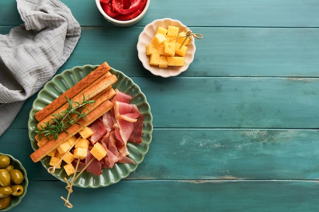 Fatias de presunto ou jamon Antipasto Deliciosos palitos de grissini com queijo presunto e azeitonas de alecrim em prato verde sobre fundo azul de madeira velho Mesa de aperitivos com lanches italianos Vista superior