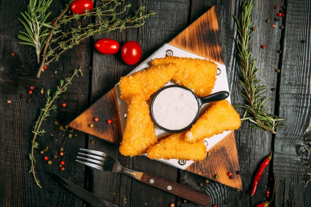 Fatias de queijo frito com molho branco em uma placa de madeira triangular