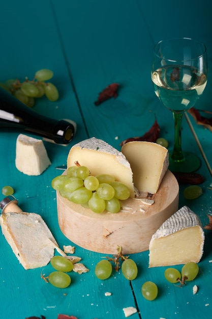 Fatias de queijo, uvas brancas, faca, vidro e uma garrafa de vinho branco sobre uma superfície de madeira. Fechar-se
