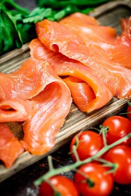 Fatias de salmão salgado com verduras e tomates em uma tábua de cortar