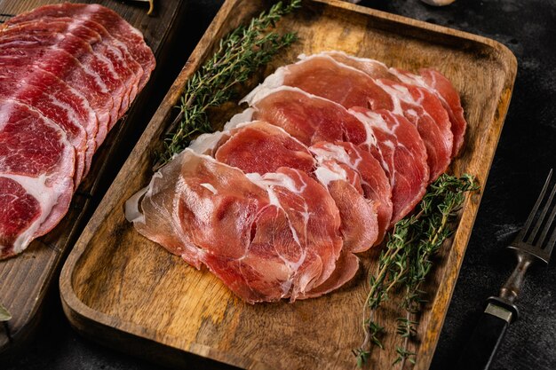 Fatias de salsicha curada seca de jamon de carne envelhecida no fundo da mesa de pedra escura preta