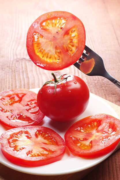 Fatias de tomate em um garfo e em um prato sobre a mesa