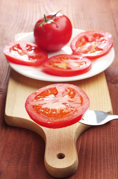 Foto fatias de tomate em um garfo e em uma tábua de cortar