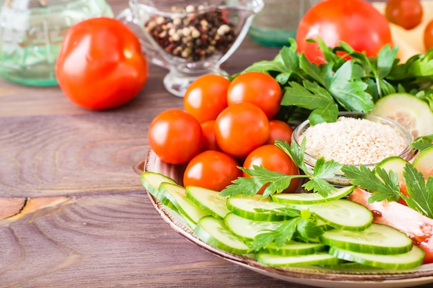 Fatias frescas de pepino, tomate, gergelim em uma tigela e salsa folhas em um prato