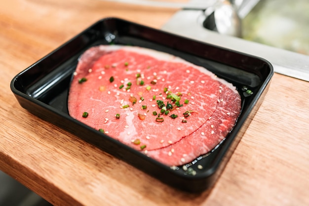 Fatias raras premium de carne Kagoshima Wagyu A5 com temporada de textura marmorizada com cebolinha picada e gergelim em um prato preto servido para Yakiniku e Shabu