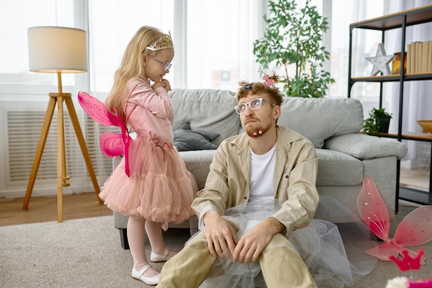 Fatiga cansada padre vestido con un disfraz divertido divirtiéndose con una hija alegre y emocionada en casa