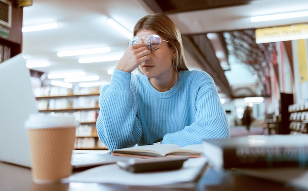 Fatiga de estudiante con dolor de cabeza y estrés de agotamiento universitario por la fecha límite del trabajo o estudio para el examen en la biblioteca Universidad del campus y cansada de estudiar con problemas de becas y dolor de salud mental