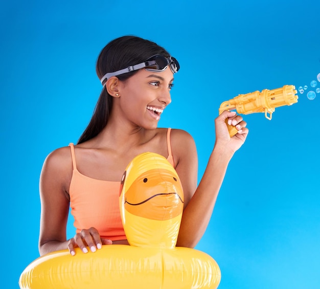 Fato de banho de verão Bubbles e mulher com arma de bolhas em um estúdio com diversão e felicidade Fundo azul isolado e modelo feminino feliz com sorriso brincalhão e roupa de natação para entretenimento na piscina