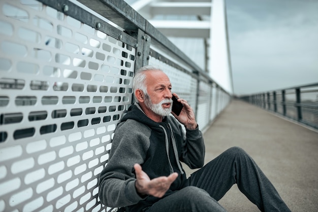 Fato de treino do homem superior que fala no telefone ao relaxar após o exercício.