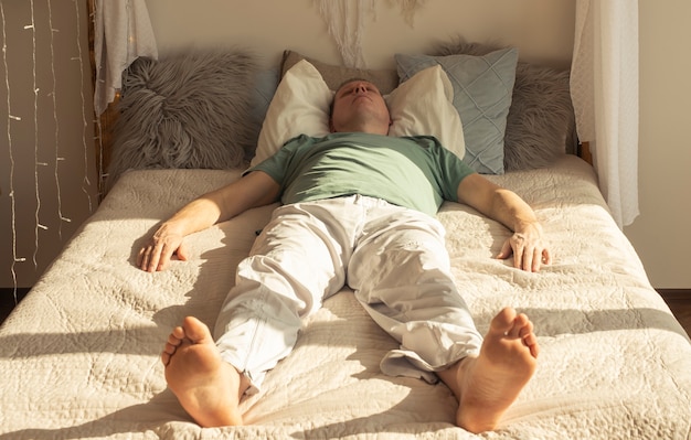 Fauler Mann, der tagsüber mit Tageslicht auf Bett im Schlafzimmer schläft oder träumt.