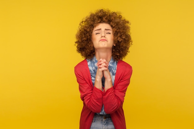 Por favor, estoy suplicando Retrato de una mujer preocupada y molesta con el pelo rizado mirando hacia arriba con una mueca implorante desesperada rezando a Dios pidiendo ayuda en un estudio interior aislado en un fondo amarillo