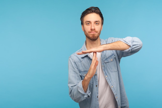 Por favor, haga una pausa. Retrato de un hombre con camisa vaquera de trabajador que muestra el tiempo de espera negándose y haciendo suficiente gesto de límite para pedir que se detenga la advertencia de la toma de estudio de fecha límite aislada en el fondo azul.