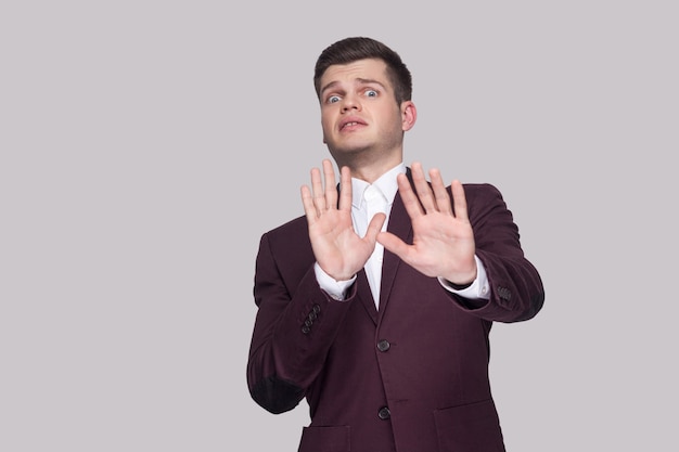 Por favor, no me toques. Retrato de joven guapo asustado en traje y camisa blanca, de pie, mirando a la cámara con miedo y bloqueando con las manos. tiro del estudio de interior, aislado en fondo gris.