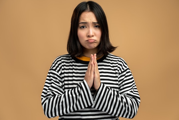 Por favor, te pido perdón. Retrato de una mujer preocupada y disgustada que mira implorando una mueca desesperada y rezando por ayuda, pidiendo disculpas. Foto de estudio aislado sobre fondo beige