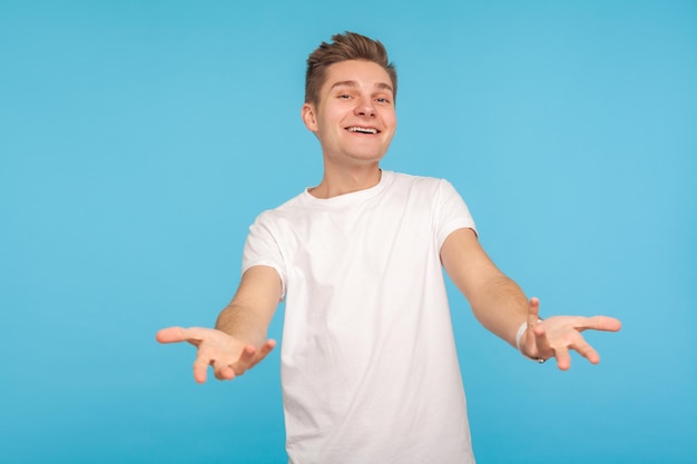 Por favor, tome gratis Retrato de un hombre generoso y amigable con una camiseta que extiende las manos como si compartiera algo de bondad y concepto de caridad en un estudio interior aislado en un fondo azul