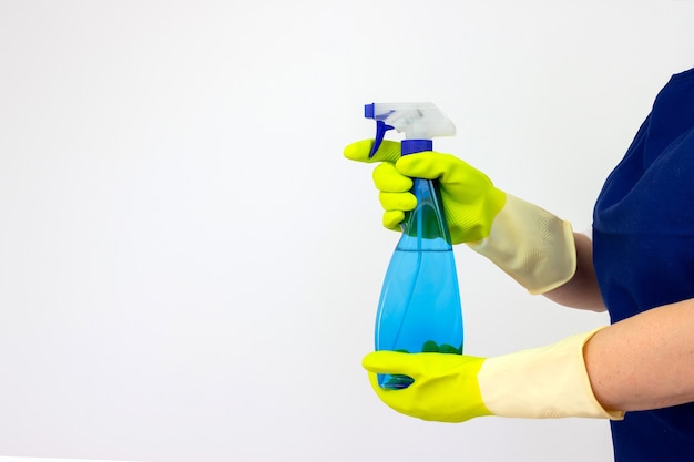 Faxineira com frasco de spray e luvas verdes sobre fundo branco. Serviço de limpeza de idéias