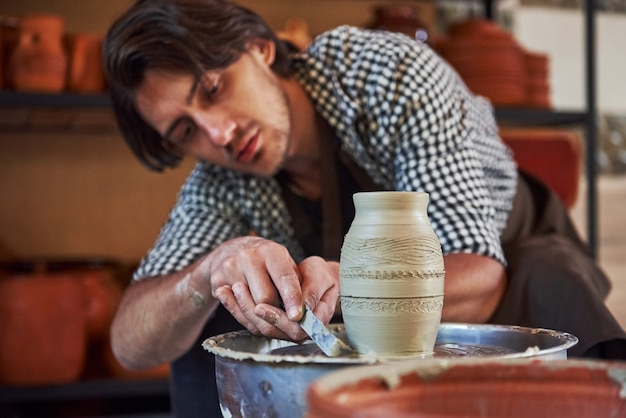 Foto faz linhas com ferramenta. o ceramista usa uma roda de oleiro e cria um produto de argila feito à mão.