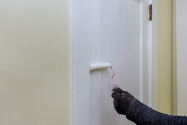 Faz-tudo, pintor de renovação doméstica de acabamento de portas usando pintura a rolo à mão com luvas