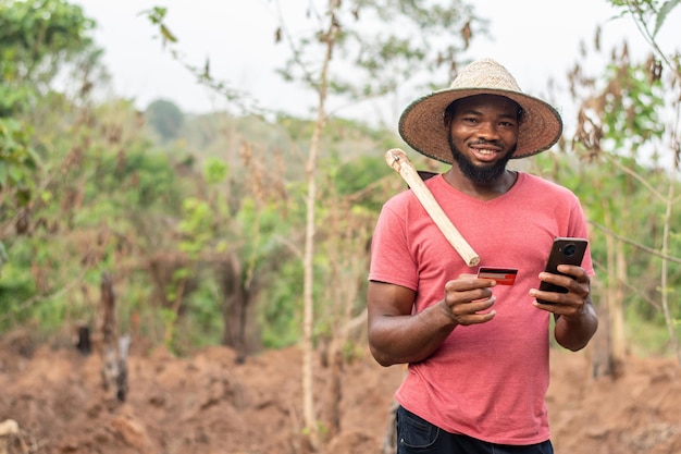 Fazendeiro africano feliz usando seu telefone e cartão de crédito