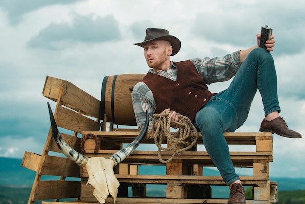 Fazendeiro de cowboy no campo usando chapéu de cowboy ocidental bebendo uísque modo masculino americano