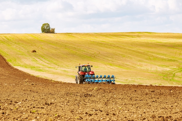 Fazendeiro em trator vermelho preparando terreno com arado para semear