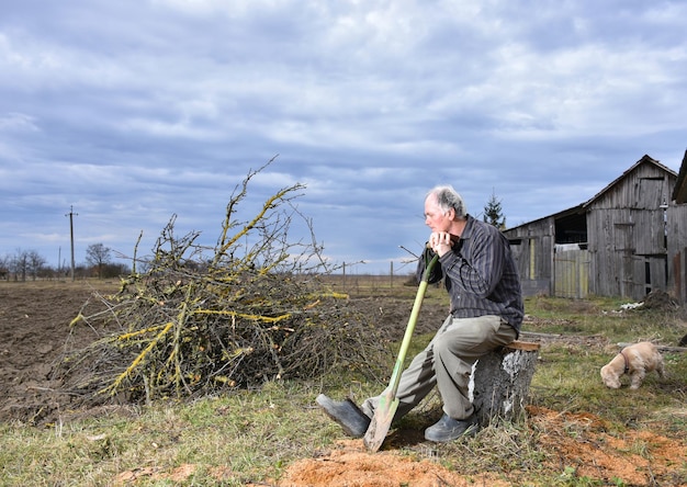 Fazendeiro sentado com uma pá no campo. Tempo de primavera. Início do trabalho de primavera no campo