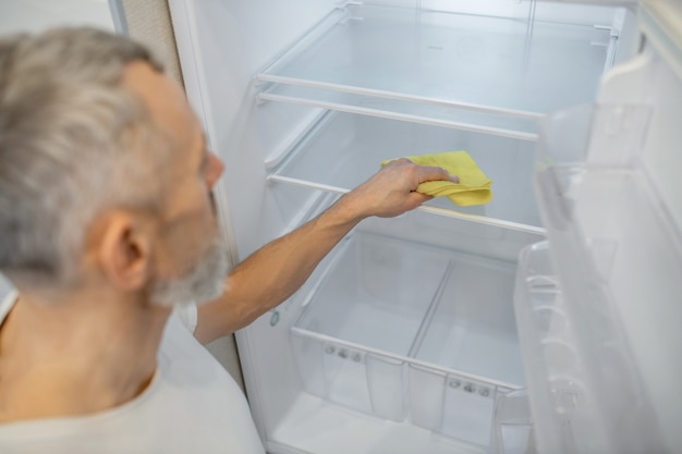 Fazendo alguma limpeza. um homem de cabelos grisalhos limpando a geladeira na cozinha