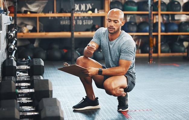 Fazendo algumas verificações ao redor do centro Foto de um jovem musculoso usando uma prancheta enquanto verifica o equipamento em uma academia