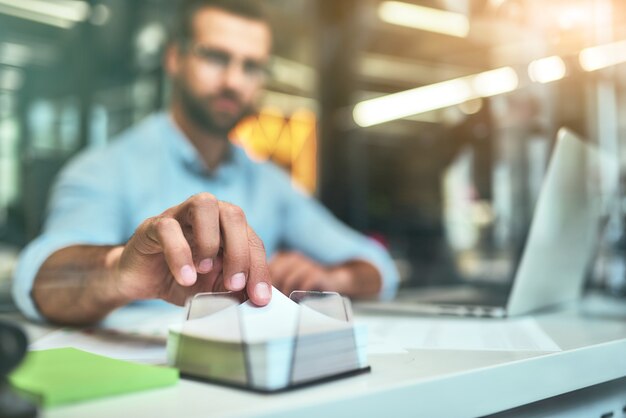 Fazendo anotações Foto desfocada de jovem empresário barbudo pegando papel branco para escrever algo