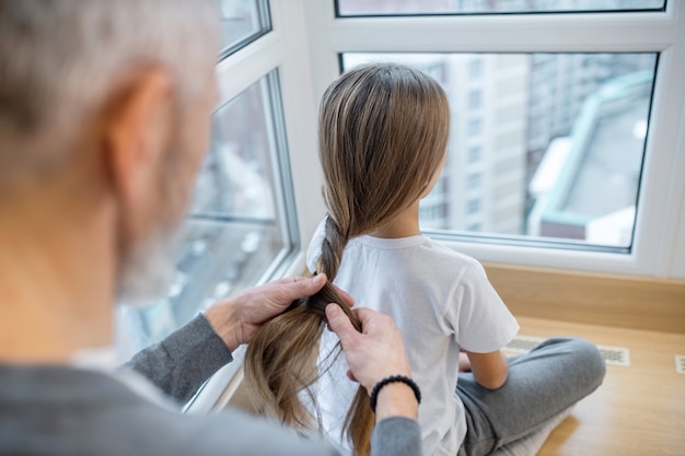 Fazendo cabelo. Um pai de cabelos grisalhos arrumando o cabelo da filha