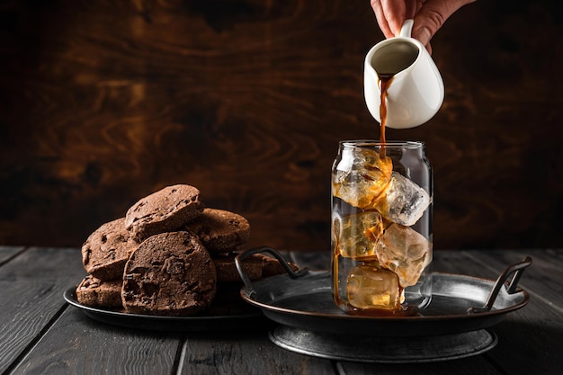 Fazendo café gelado. despejando café preto de um jarro de leite em um copo. biscoitos de chocolate em um prato.