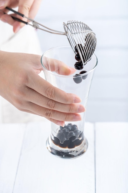 Fazendo colher de chá de bolhas e despeje bolas de bolhas de tapioca sabor açúcar mascavo cozido no copo no fundo da mesa de madeira branca feche o espaço da cópia