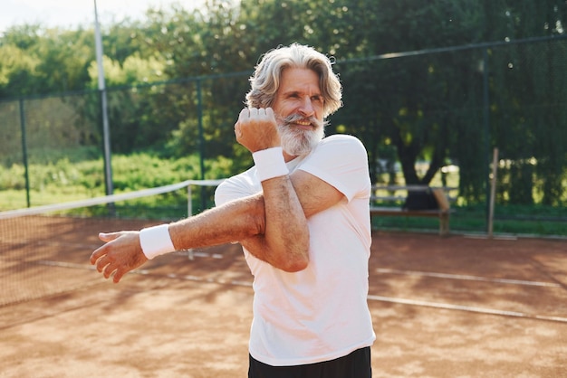 Fazendo exercícios de aquecimento Homem elegante moderno sênior ao ar livre no campo esportivo durante o dia