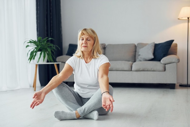 Fazendo exercícios de fitness Mulher sênior com cabelo loiro está em casa