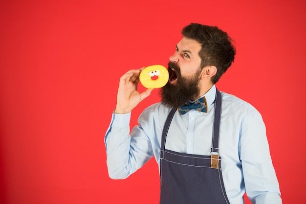 Fazendo lanches Dieta e comida saudável Padeiro come rosquinha Chef man no café Caloria Sinta fome Padeiro barbudo Homem barbudo no avental padeiro segure rosquinha Hipster engraçado Padeiro profissional