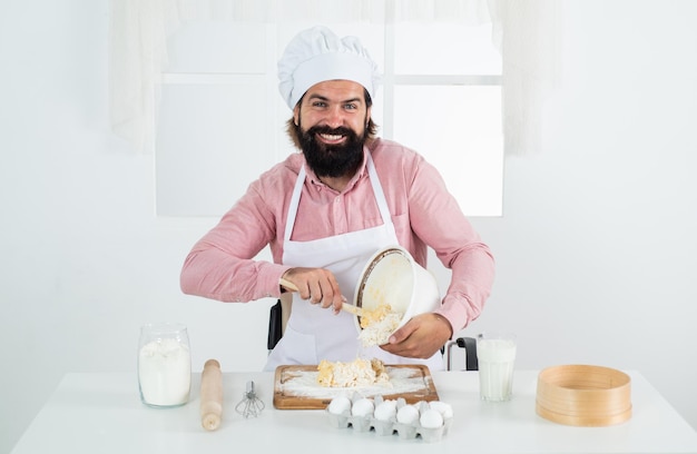 Fazendo massa fresca alegre homem barbudo usar chapéu de chef cozinheiro masculino preparando comida na cozinha em casa hipster brutal no avental cozinhar hora da refeição para comer o conceito de cozimento feliz de limpeza