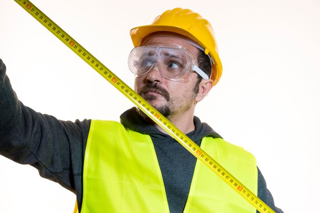 fazendo medições com um medidor, um homem que quer fazer um trabalho sem conhecimento, um trabalho sem experiência. Faça você mesmo, homem vestido com capacete de construtor amarelo com óculos de proteção prontos para começar