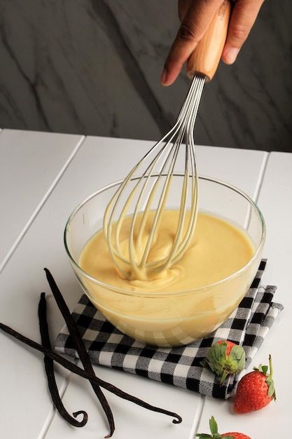 Fazendo panquecas, bolo, mãos de padeiro despejando a massa e batendo a massa na tigela. Conceito de cozinhar ingredientes e método em fundo branco de madeira, receitas de sobremesas e comida caseira.