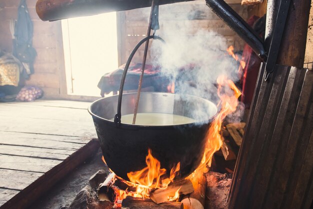 Fazendo queijo orgânico em casa de montanha de madeira. As pessoas vivem aqui no verão, vacas leiteiras, que estão a pasto, fervem o queijo no fogo aberto. Capturado em 15 de novembro de 2015 nas montanhas dos Cárpatos / Ucrânia