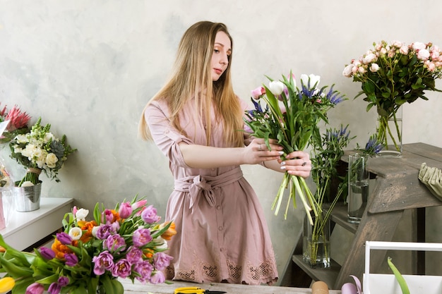 Fazendo ramo de primavera na floricultura. Florista montando bouquet tenro com tulipa branca, peônia fresca e flores silvestres. Oficina de decoradores