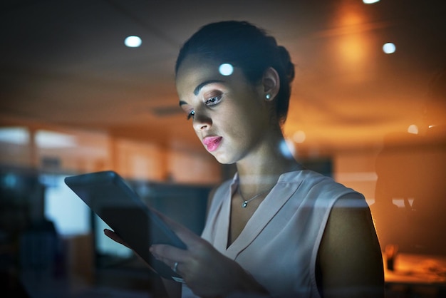 Fazendo seu trabalho duro se traduzir em sucesso Foto de uma jovem empresária usando um tablet no escritório à noite