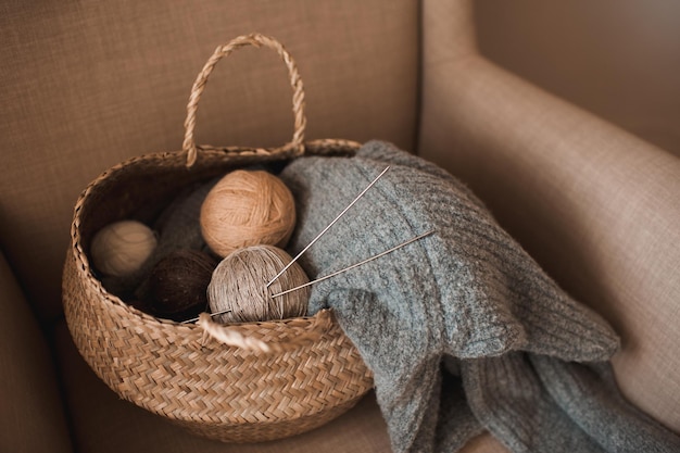 Fazendo suéter de malha caseiro em casa Cesta de palha com novelo de lã de fios com tecido de malha na poltrona dentro de casa Tendo hobby Atmosfera aconchegante de hygge no quarto