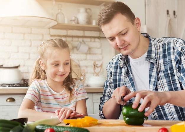 Fazendo surpresa agradável para a mãe: linda garotinha ajudando o pai, cortando pimenta para a salada, copiando espaço