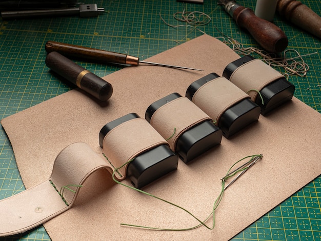 Fazendo um estojo de couro para baterias por um curtidor, em um tapete verde auto-cicatrizante, conceito de artesanato em couro