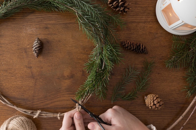 Fazendo uma guirlanda de natal com abetos e cones em uma mesa de madeira